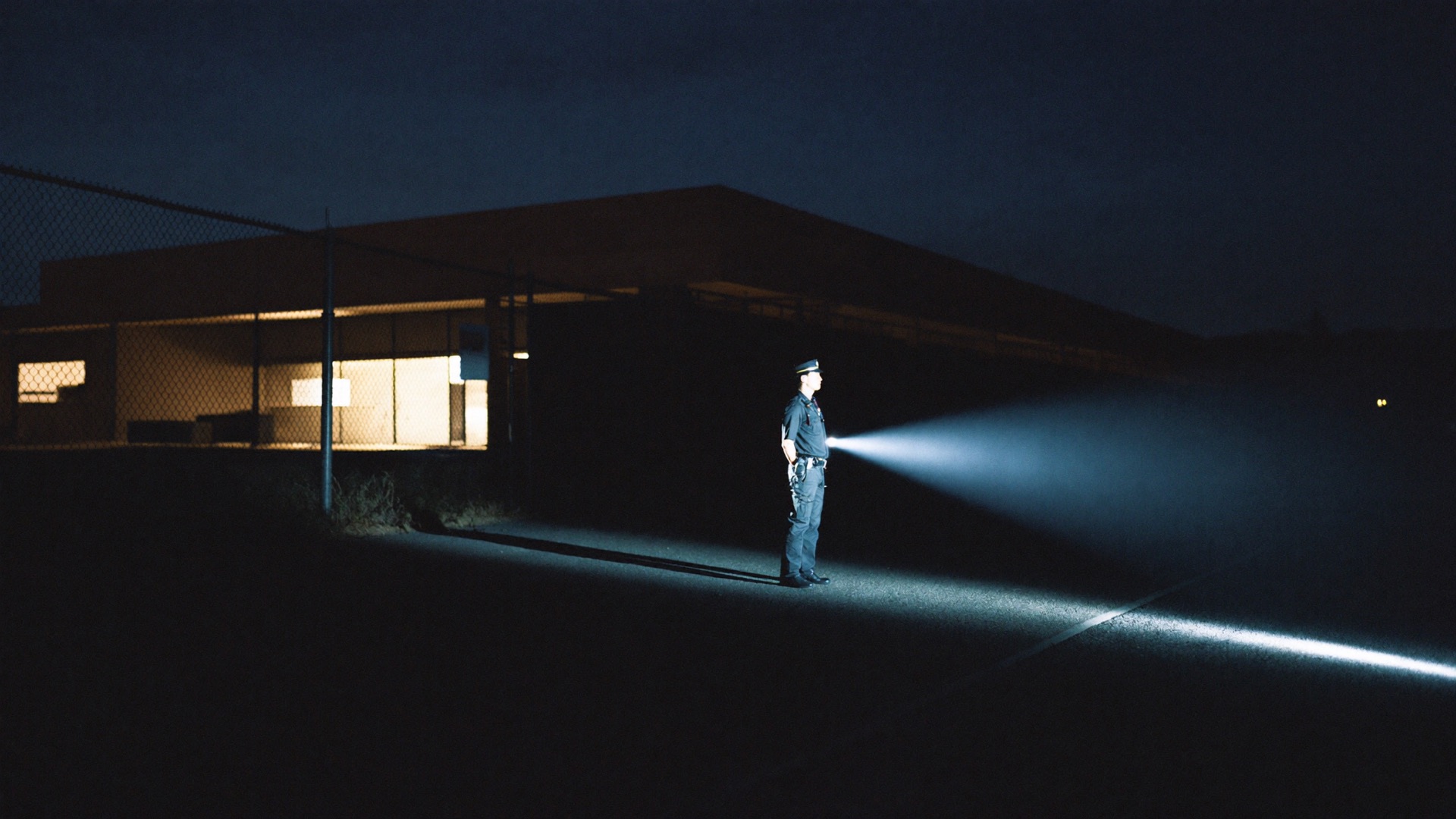 A lone officer sweeps a commercial yard with a flashlight at 2 AM.